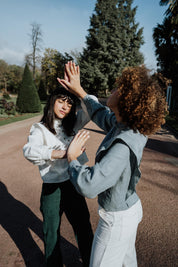Zwei Frauen tragen die Margaret-Bluse, eine in schieferblauem Leinen und die andere in weißem Leinen. Sie sind im Freien, im Park.