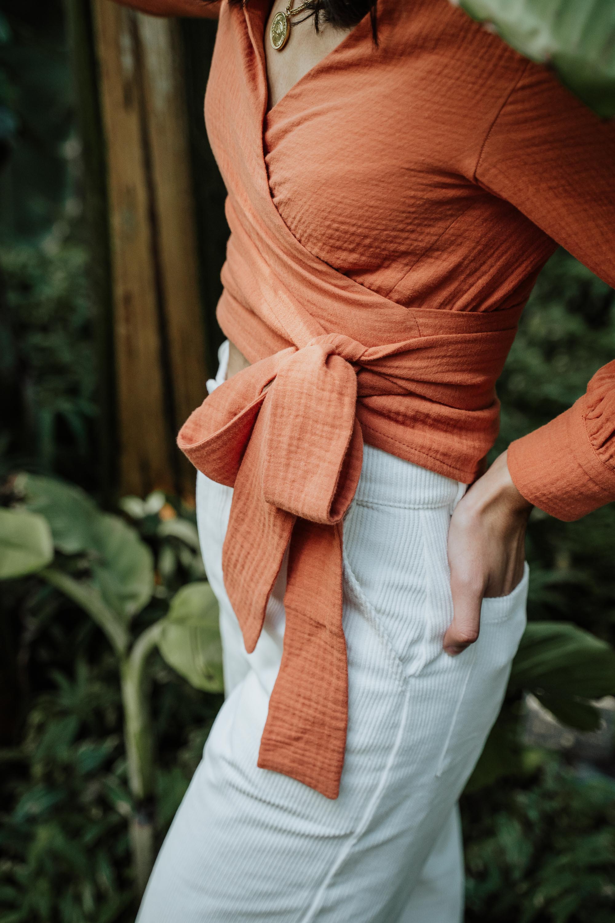 Nahaufnahme des Cache-Cœur Uluru in Terrakotta, getragen von einer Frau, zeigt das elegante Design und die praktische Schleife um die Taille.