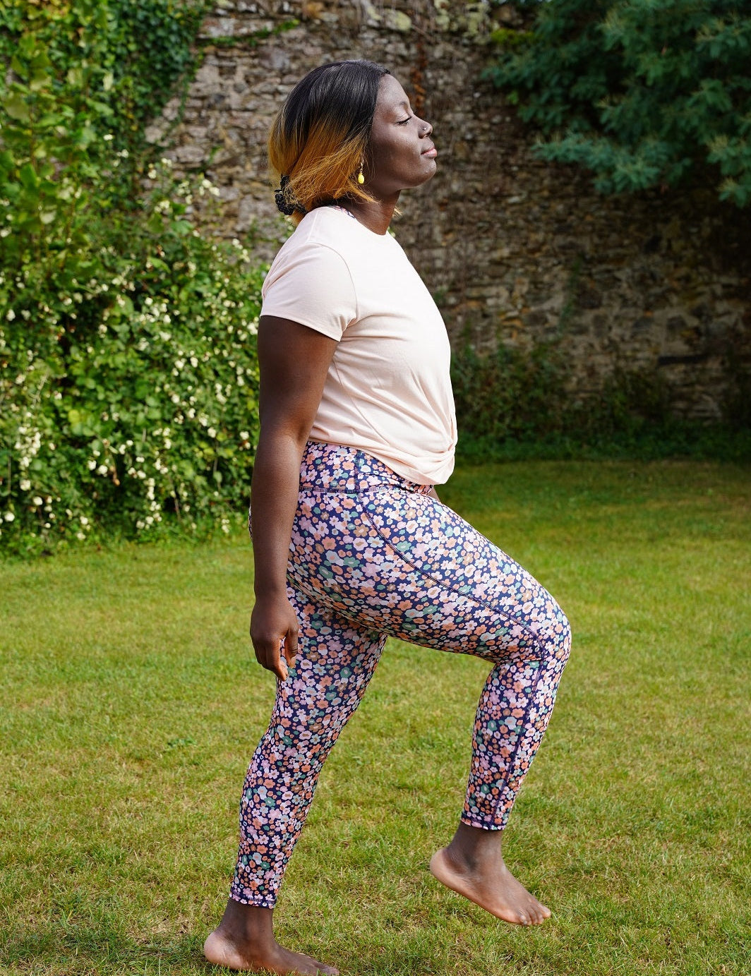 Frau macht Fitnessübungen im Park mit den recycelten ‘Colibri’-Leggings mit Blumenmotiv für maximale Bewegungsfreiheit