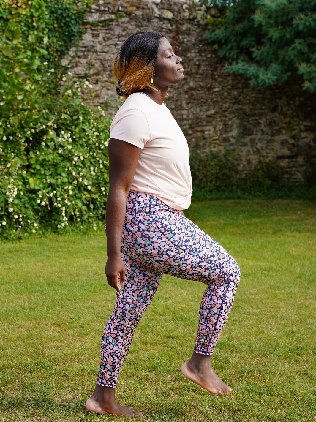 Frau macht Fitnessübungen im Park mit den recycelten ‘Colibri’-Leggings mit Blumenmotiv für maximale Bewegungsfreiheit