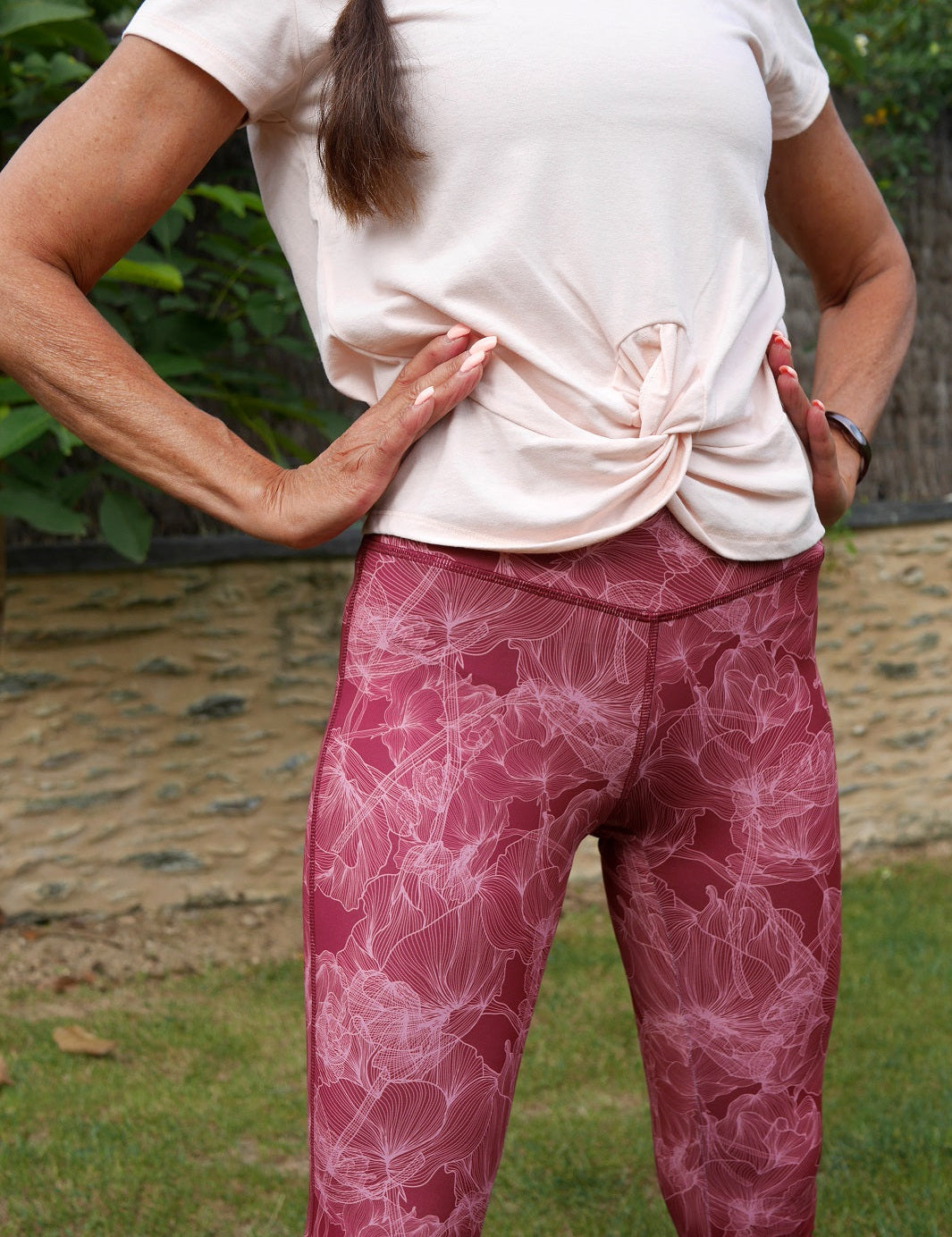 Frau im Yoga-Outfit in der Natur, trägt Bordeaux Colibri-Leggings mit Blumenmotiv, elegant und funktionell