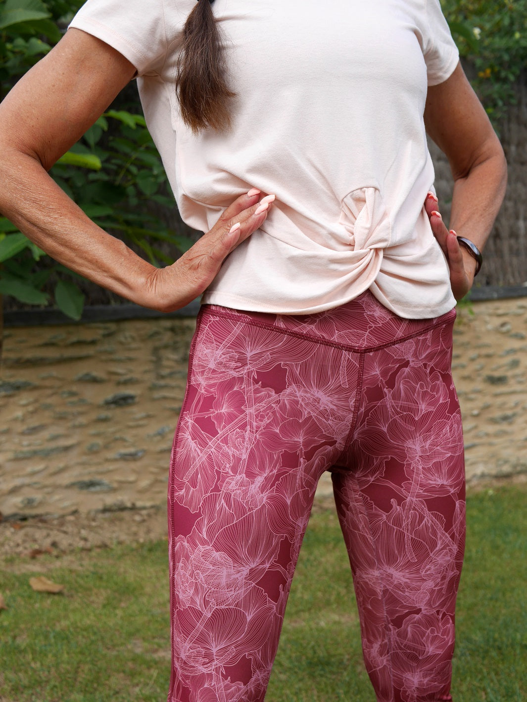 Frau im Yoga-Outfit in der Natur, trägt Bordeaux Colibri-Leggings mit Blumenmotiv, elegant und funktionell