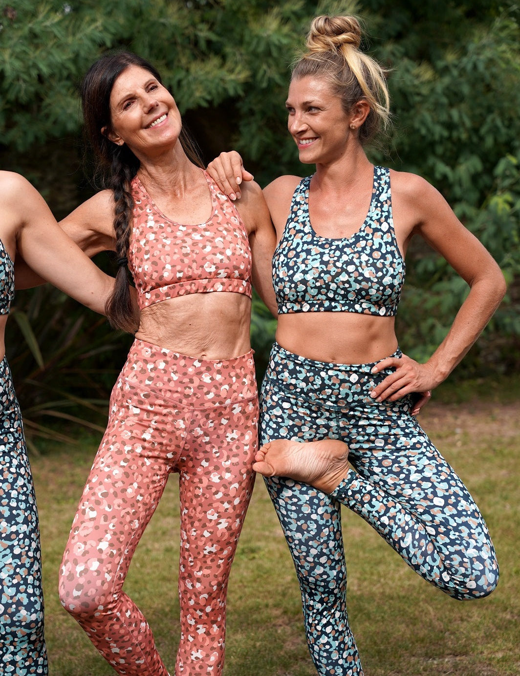 Zwei Frauen in der Natur, zeigen die Colibri-Leggings in rosa und grüner Panther-Optik beim Yoga