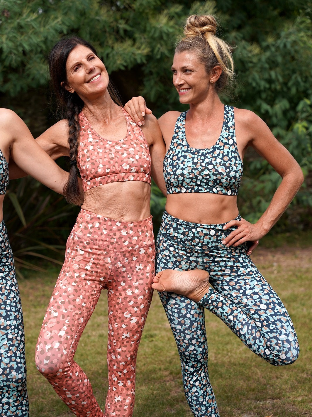 Zwei Frauen in der Natur, zeigen die Colibri-Leggings in rosa und grüner Panther-Optik beim Yoga