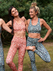 Zwei Frauen in der Natur, zeigen die Colibri-Leggings in rosa und grüner Panther-Optik beim Yoga