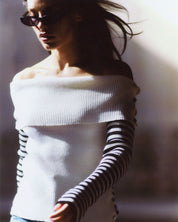 Lifestyle-Aufnahme einer Frau im écrufarbenen Merinopullover Céphée – leichter Bardot-Ausschnitt und feiner Rippstrick für feminine Looks.