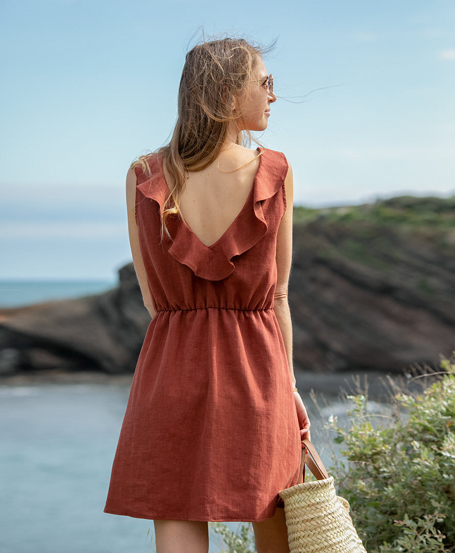 Rückenansicht des Kleids "Mathilde" am Meer. Terrakottafarbenes Sommerkleid aus 100 % Leinen mit elegantem Rückenausschnitt