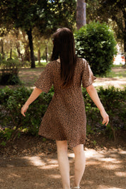 Frau im Sommerkleid mit Leo-Print von hinten, elegant im Park – nachhaltige EcoVero™-Viskose, eleganter Schnitt und femininer V-Ausschnitt für zeitlose Mode.