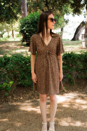 Frau im Sommerkleid mit Leo-Print, geht durch einen schattigen Parkweg  – elegante, umweltfreundliche Mode aus EcoVero™-Viskose für moderne Frauen, ideal für sonnige Sommertage.