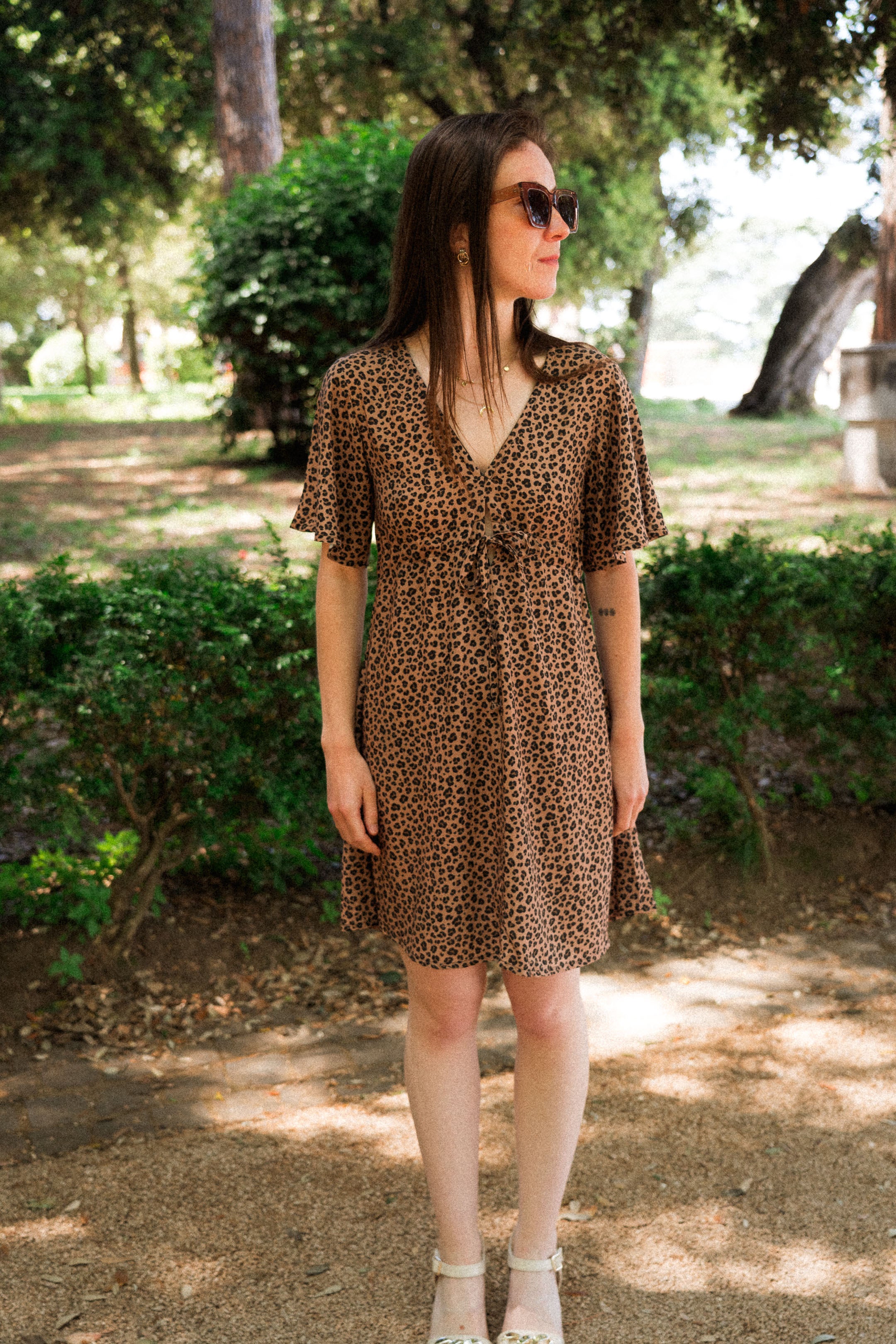 Frau im Sommerkleid mit Leo-Print, geht durch einen schattigen Parkweg  – elegante, umweltfreundliche Mode aus EcoVero™-Viskose für moderne Frauen, ideal für sonnige Sommertage.