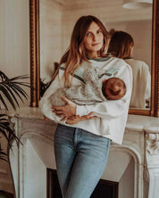 Entspannter Stillmoment mit dem Still-Sweatshirt Chloé. Die seitlichen Reißverschlüsse ermöglichen ein diskretes Stillen, während die Mutter sich bequem an einen Kamin lehnt.