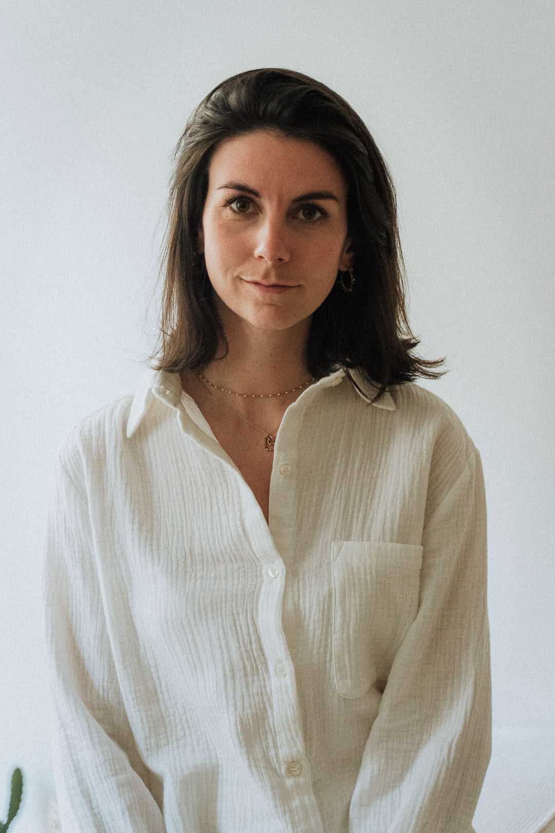 Eine Frau trägt die weiße Bluse Noosa aus Baumwollgaze. Die Bluse besticht durch ihren zeitlosen Stil und die edlen Details.