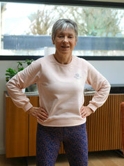 Frau trägt das 'Héron' Sweatshirt in Rosa im Innenbereich, bequem und stilvoll.
