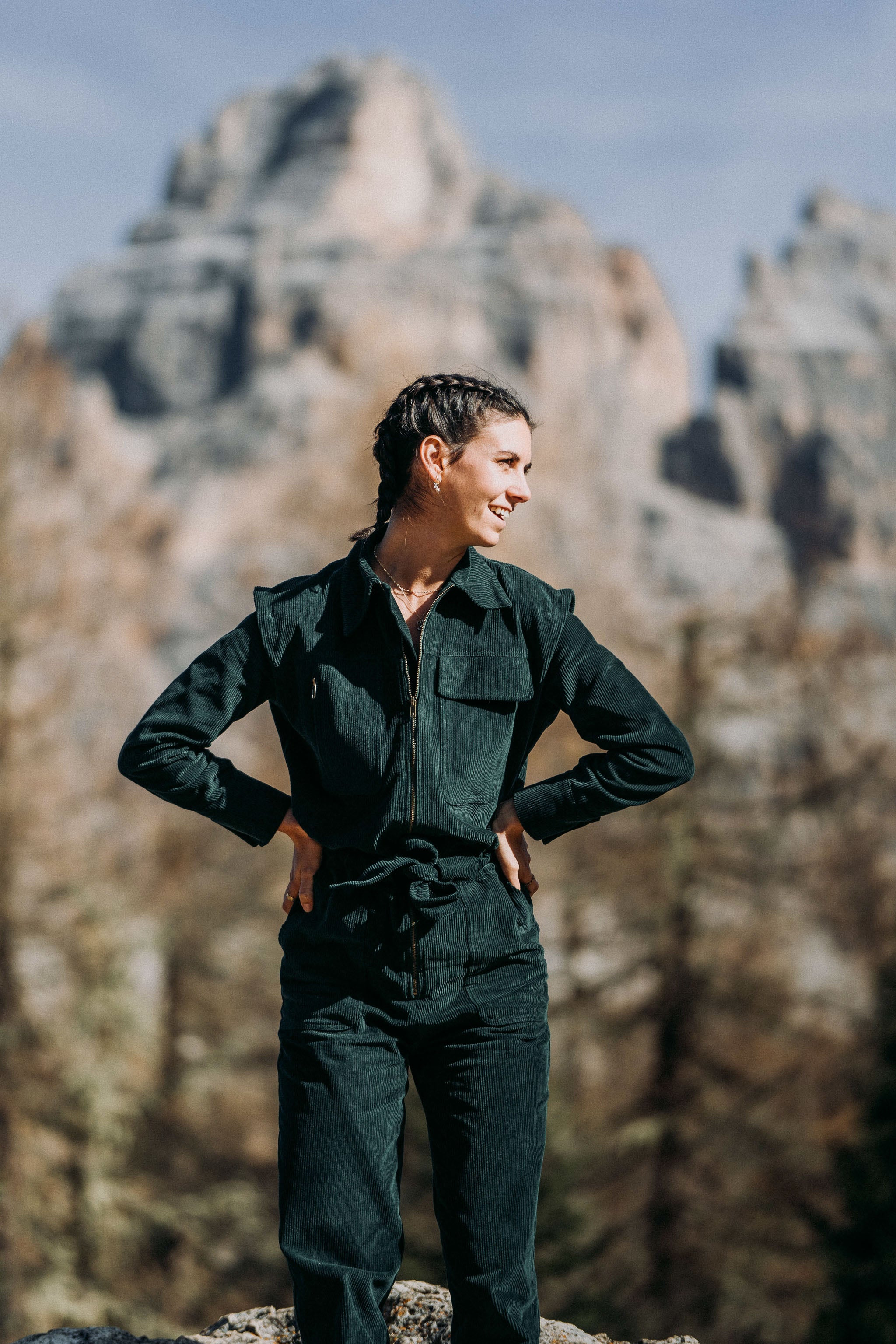 Frau trägt den grünen Baumwollcord-Einteiler Dolomites inmitten einer malerischen Berglandschaft, ideal für einen stilvollen und bequemen Look.