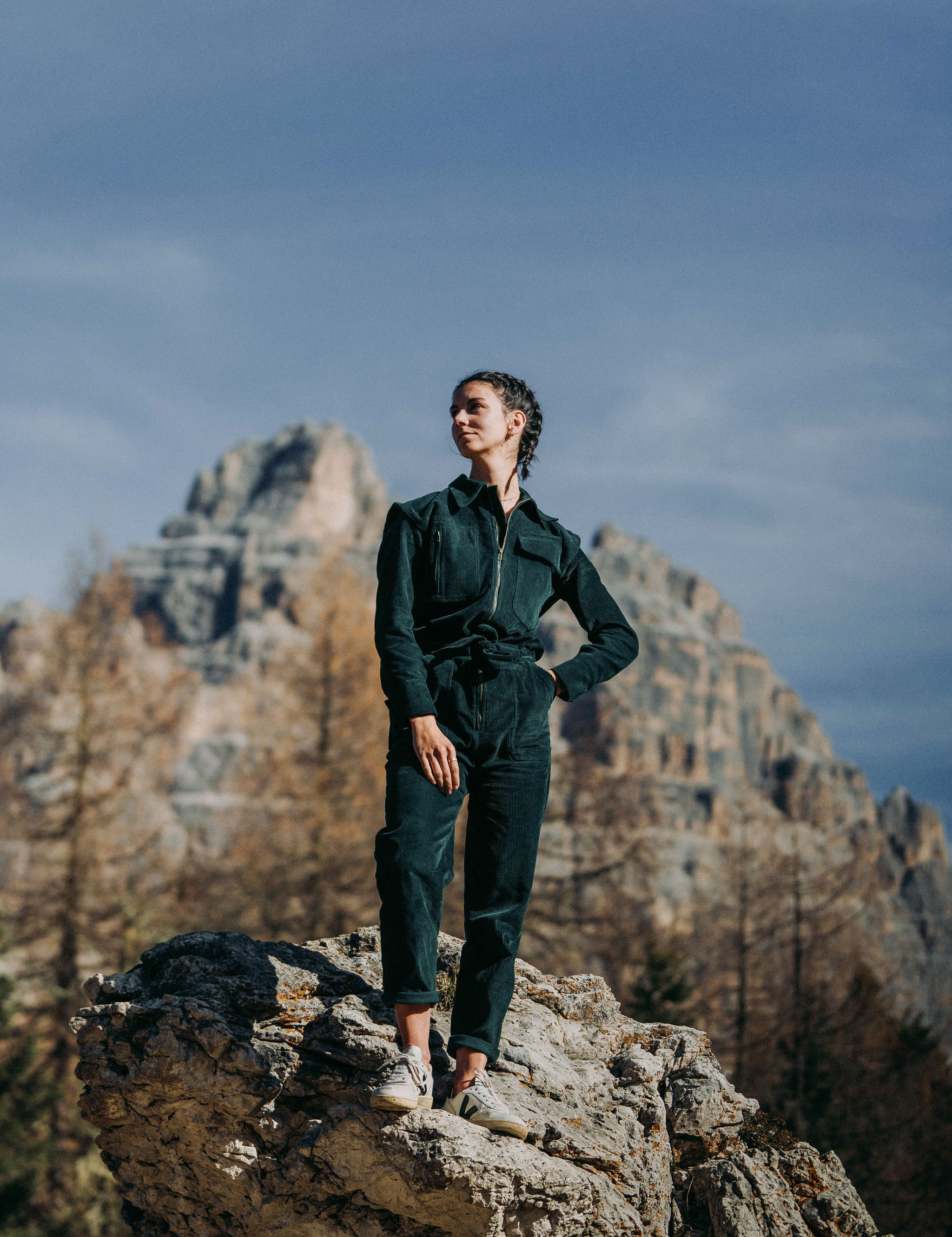Frau trägt den grünen Einteiler Dolomites aus Baumwollcord in den Bergen, umgeben von malerischen Felsen und grüner Landschaft.