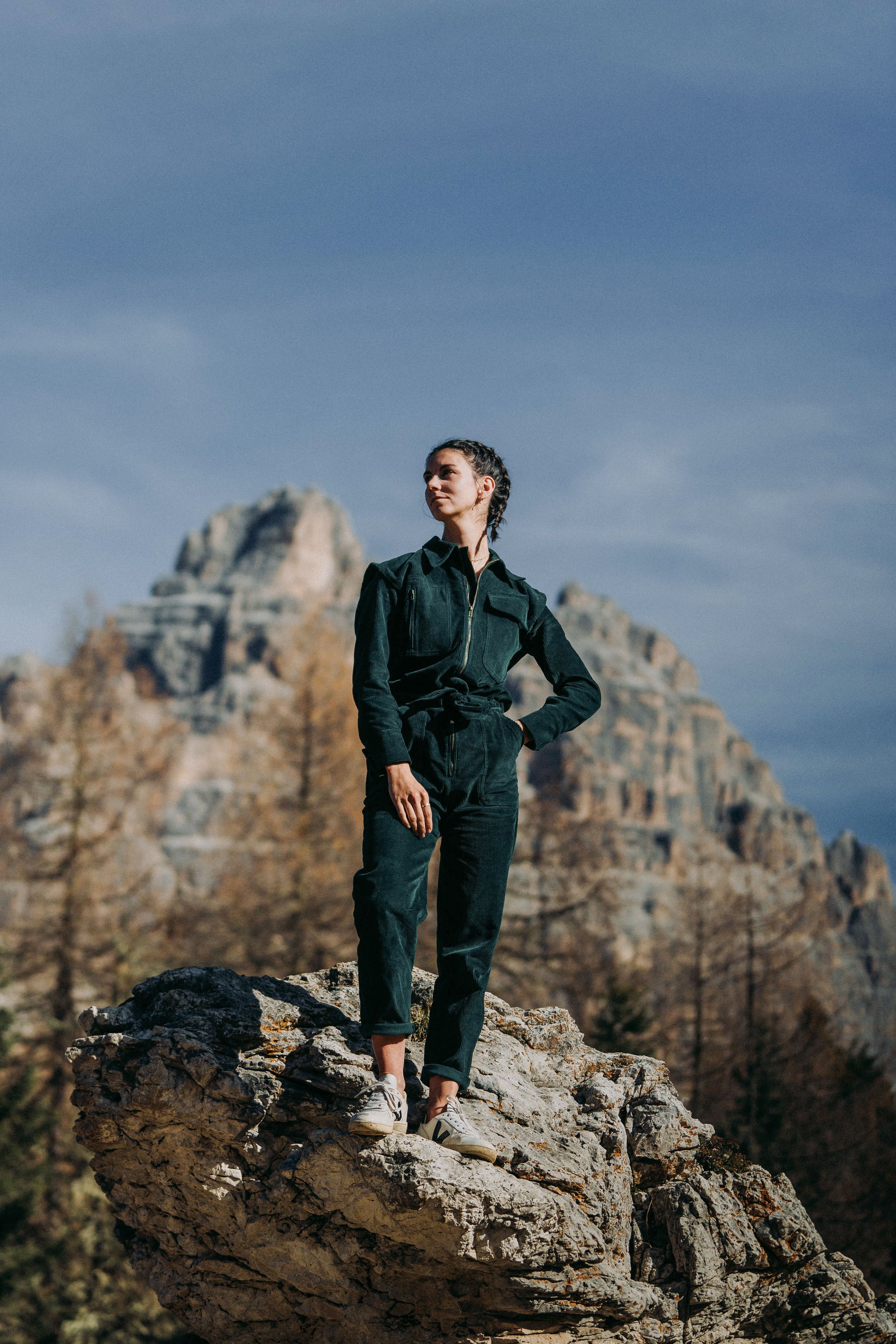 Frau trägt den grünen Einteiler Dolomites aus Baumwollcord in den Bergen, umgeben von malerischen Felsen und grüner Landschaft.