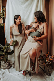 Zwei Frauen im Stillkleid Noémie – eine stillt diskret ihr Baby, während die andere das elegante Sommerdesign präsentiert.