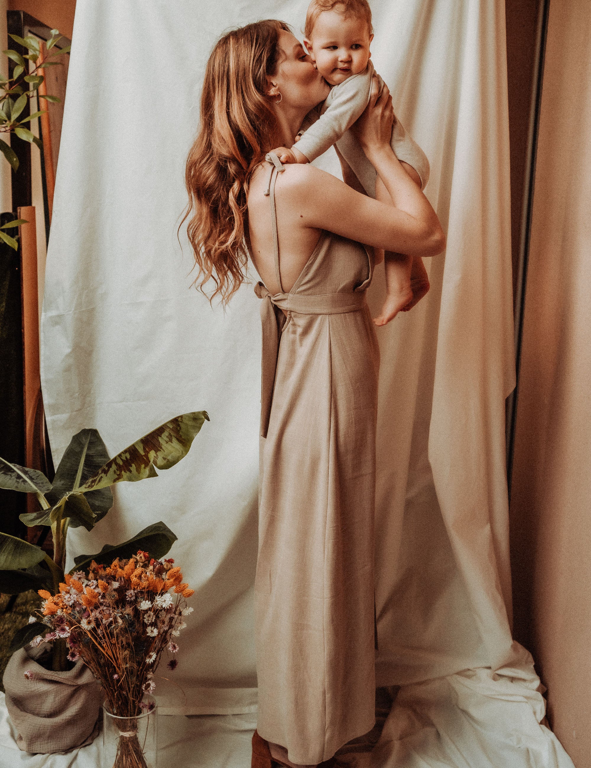 Mutter in Sommerkleid Noémie in Beige, trägt ihr Baby liebevoll im Arm – stilvoll, feminin und stillfreundlich zugleich.