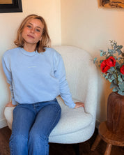 Frau im Sessel mit dem Stillpullover Mimosa – eleganter Alltagslook im Oversize-Schnitt, Babyblau.