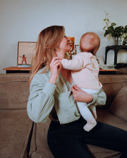 Moderne Stillbluse Tiphaine in Aqua-Grün – Mutter sitzt mit ihrem Baby, trägt eine luftige Bluse aus Bio-Baumwolle.