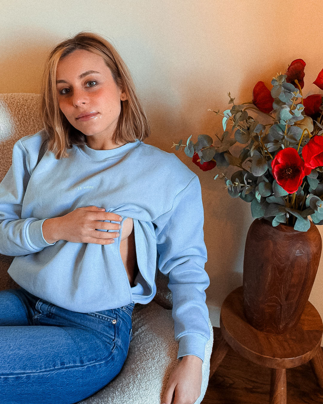 Frau im Sessel zeigt die diskreten Stillöffnungen des Pullovers Mimosa – reißverschlussfrei und dezent integriert.