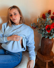Frau im Sessel zeigt die diskreten Stillöffnungen des Pullovers Mimosa – reißverschlussfrei und dezent integriert.