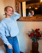 Frau steht und trägt den Stillpullover Mimosa in Babyblau – moderner Oversize-Schnitt, ohne Reißverschluss.
