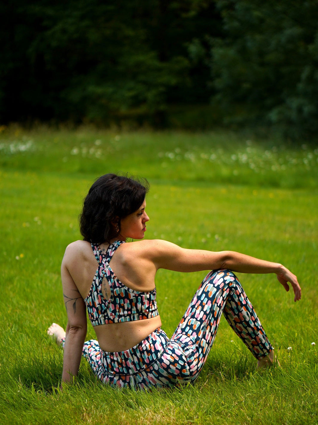Frau sitzt im Gras mit COLIBRI-Leggings im grafischen Buntmotiv – weiches, elastisches Material für maximale Bewegungsfreiheit.