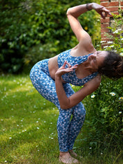 Eine Frau praktiziert Yoga im Freien, trägt den COLIBRI-Leggings und das MÉSANGE-Sport-Bustier mit Margeriten-Motiv.