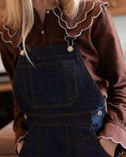 Nahaufnahme der Vorderseite einer dunkelblauen Denim-Latzhose mit Nähten und Tasche