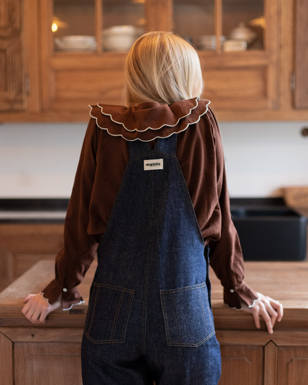 Rückansicht einer Frau in dunkelblauer Denim-Latzhose mit verstellbaren Trägern