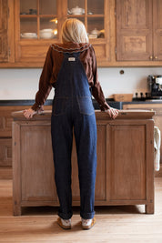 Frau von hinten in dunkelblauer Latzhose aus Denim, klare Linien und hohe Taille sichtbar