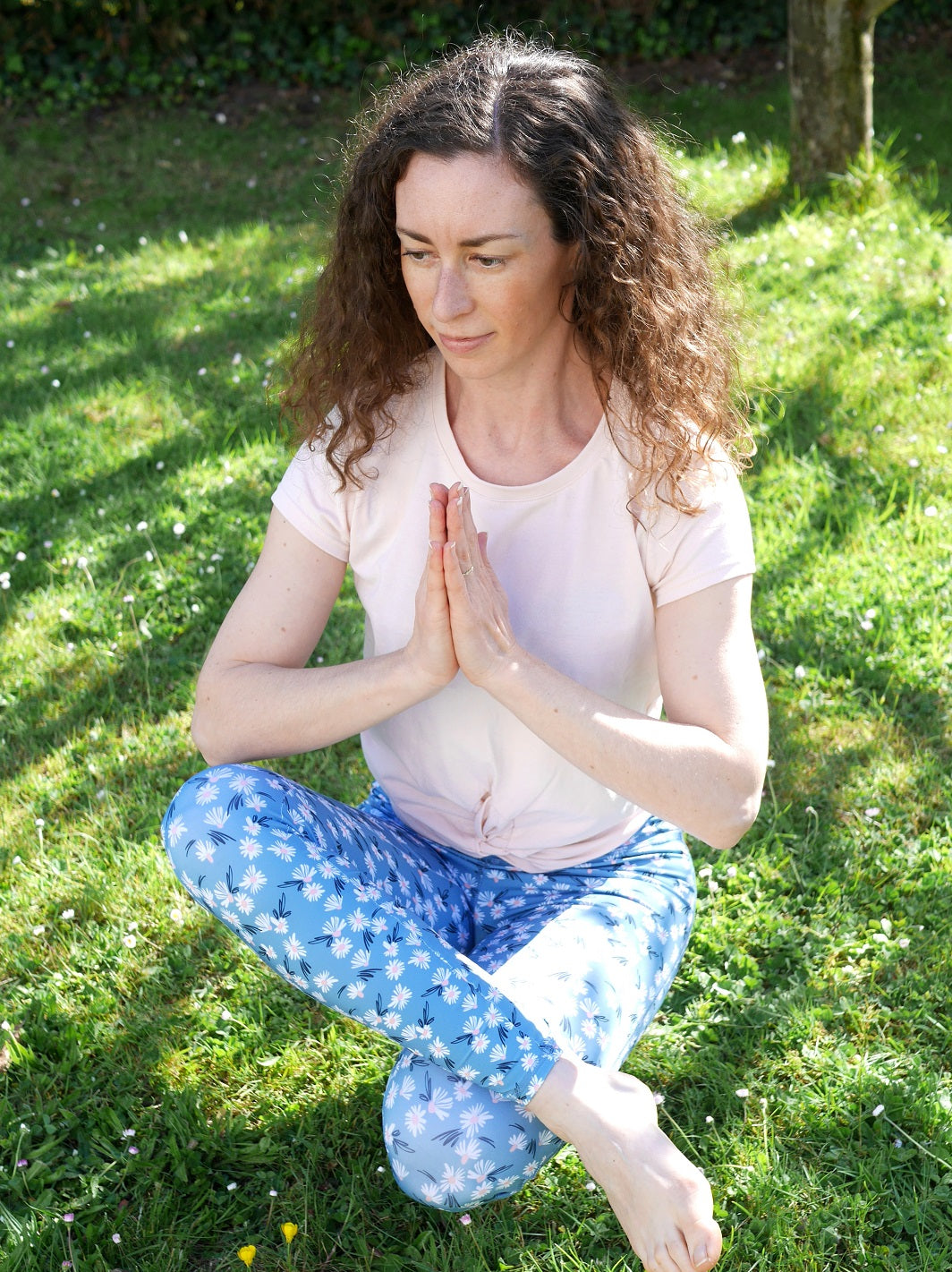 Frau in Yoga-Pose im Freien trägt den farbenfrohen COLIBRI-Leggings mit Margeriten-Motiv – flexibel und atmungsaktiv für intensive Workouts.