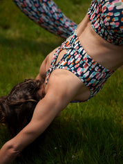 Frau in Yoga-Pose draußen, trägt das MÉSANGE-Sport-Bustier mit grafischem Buntmotiv und Legging, komfortabel und stylisch für Pilates, Yoga oder Fitnessübungen im Freien.