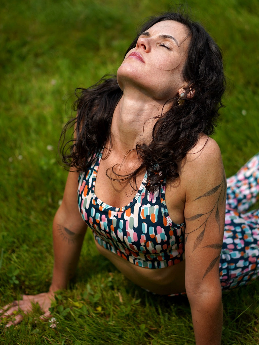 Frau trägt das MÉSANGE-Sport-Bustier mit grafischem Buntmotiv und passendem Legging beim Yoga draußen, nachhaltige Fitness-Mode aus recyceltem Polyester.