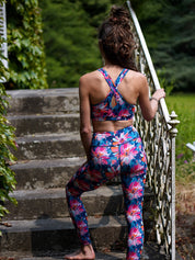 Frau trägt das MÉSANGE Sport-Bustier mit Lotusblüten-Motiv und die passende COLIBRI-Leggings im Freien, Rückenansicht, zeigt die eleganten gekreuzten Träger und den harmonischen Look für Yoga und Pilates.