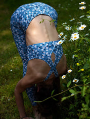 Frau beim Yoga draußen in einer dynamischen Pose, trägt das Sport-Bustier Mésange Margeriten-Motiv und passendes Leggings.