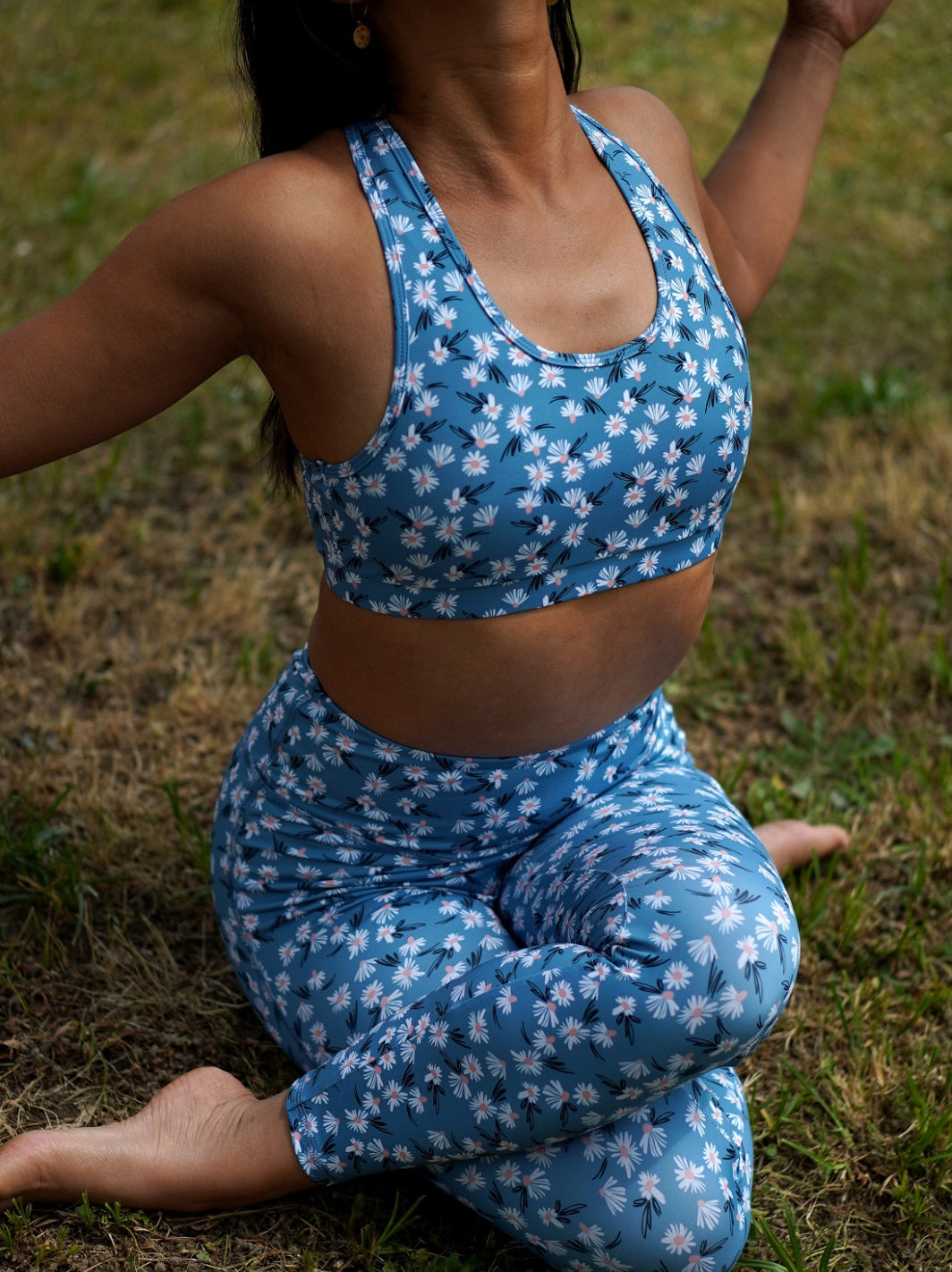 Frau sitzt im Gras beim Yoga draußen, trägt das Sport-Bustier Mésange Margeriten-Motiv und passendes Leggings.