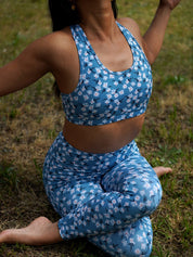 Frau sitzt im Gras beim Yoga draußen, trägt das Sport-Bustier Mésange Margeriten-Motiv und passendes Leggings.