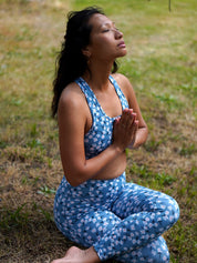 Frau übt Yoga draußen, trägt das Sport-Bustier Mésange Margeriten-Motiv und das passende Leggings, Seitenansicht.