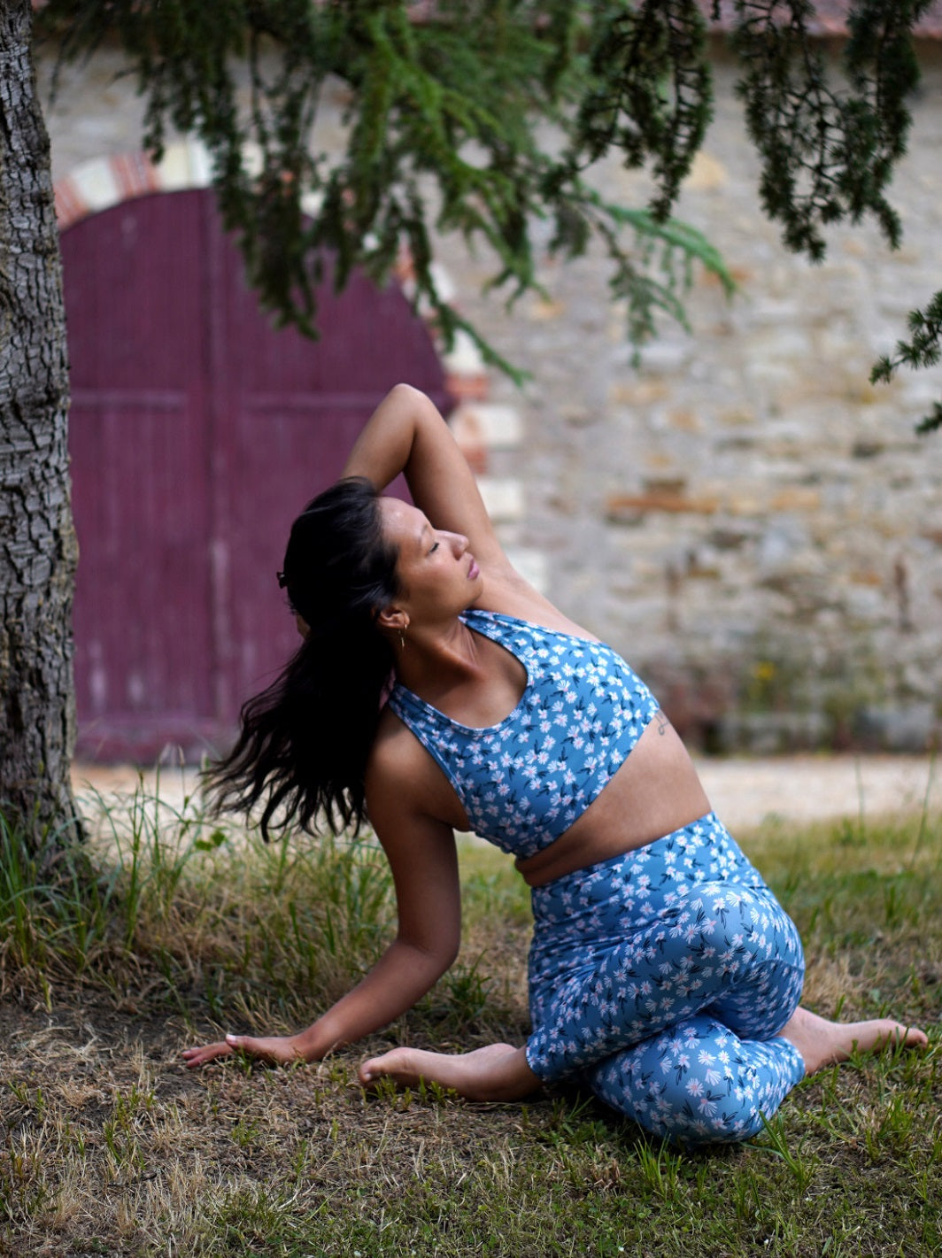 Frau trägt das Sport-Bustier Mésange mit Margeriten-Motiv und passendem Leggings beim Yoga im Freien, frontal aufgenommen.