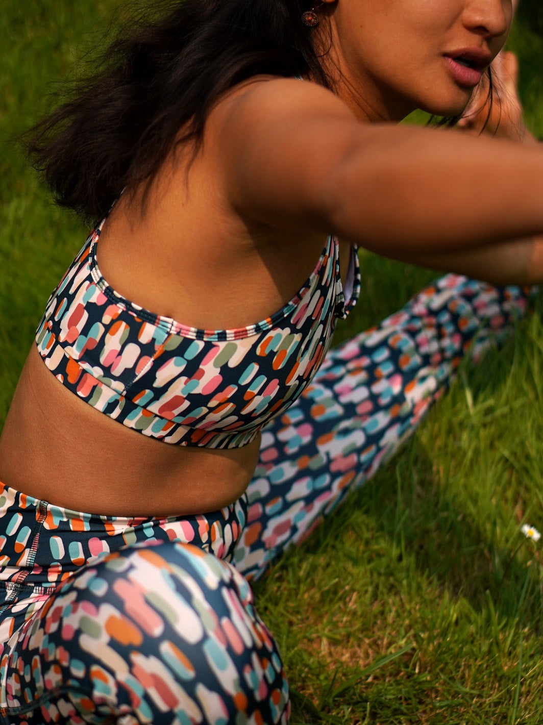 Seitenansicht der Frau in der Natur, sie trägt das MÉSANGE-Sport-Bustier mit grafischem Buntmotiv und Legging, ideal für Yoga, Pilates und Fitnessübungen.