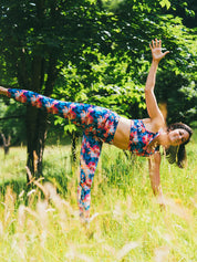 Frau trägt Sport-Bustier und Legging mit Lotusblüten-Motiv und macht Yoga im Freien.