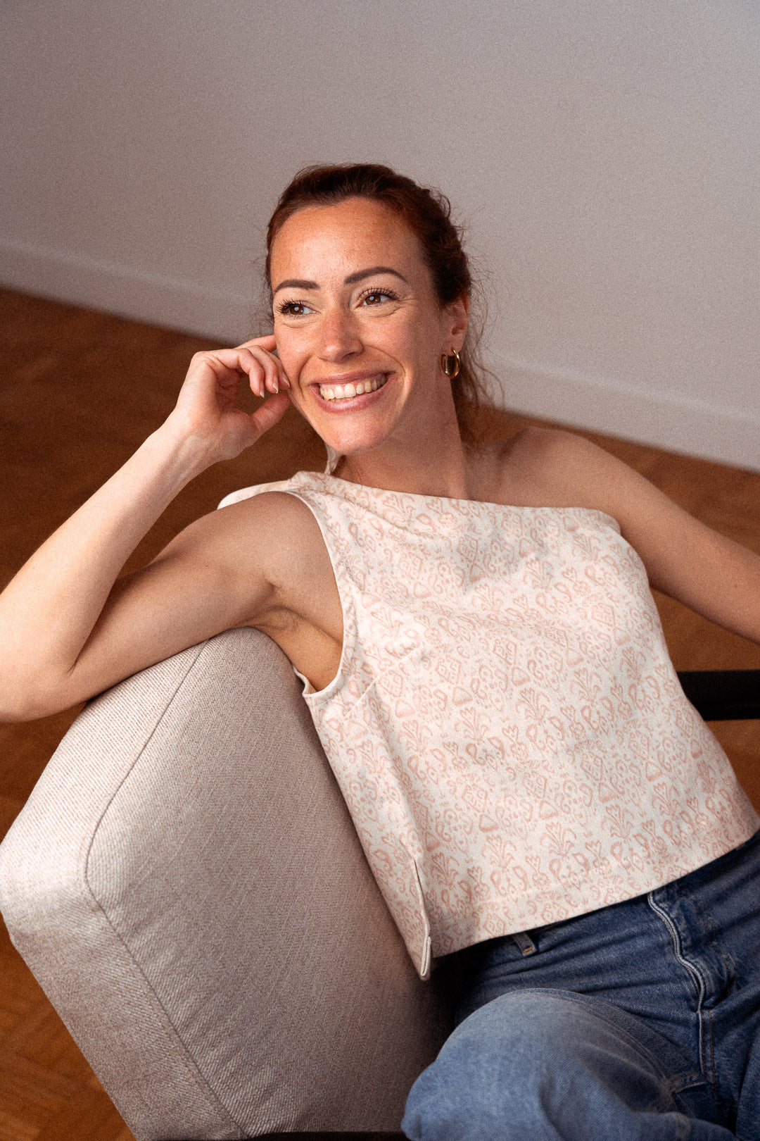 Frau sitzt elegant auf einem Sessel und trägt das asymmetrische Top "Luce" aus recycelter Baumwolle – stilvolle Damenmode im französischen Look, nachhaltig und lokal gefertigt.